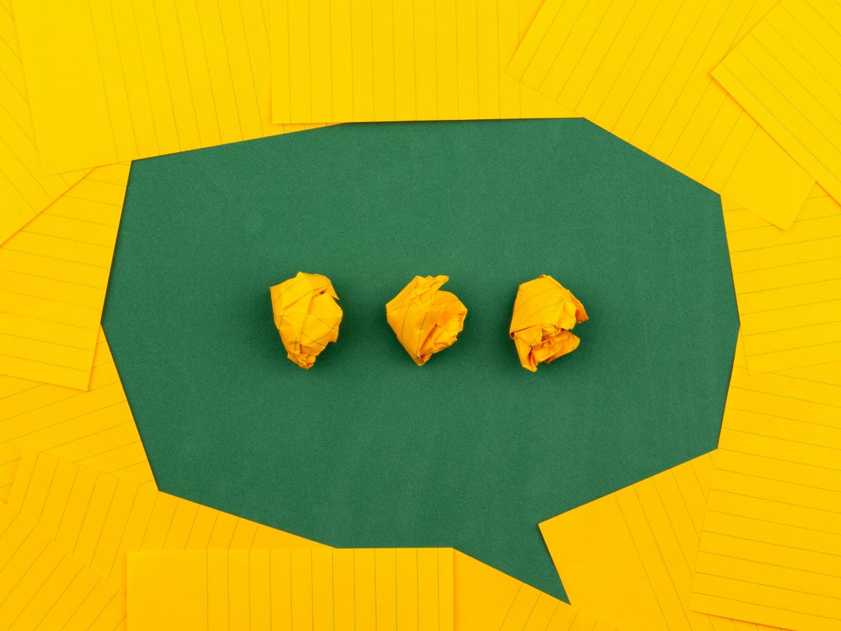 A green speech bubble made with yellow lined paper on top of plain green paper. three rolled up bit of yellow paper in the middle of the speech bubble